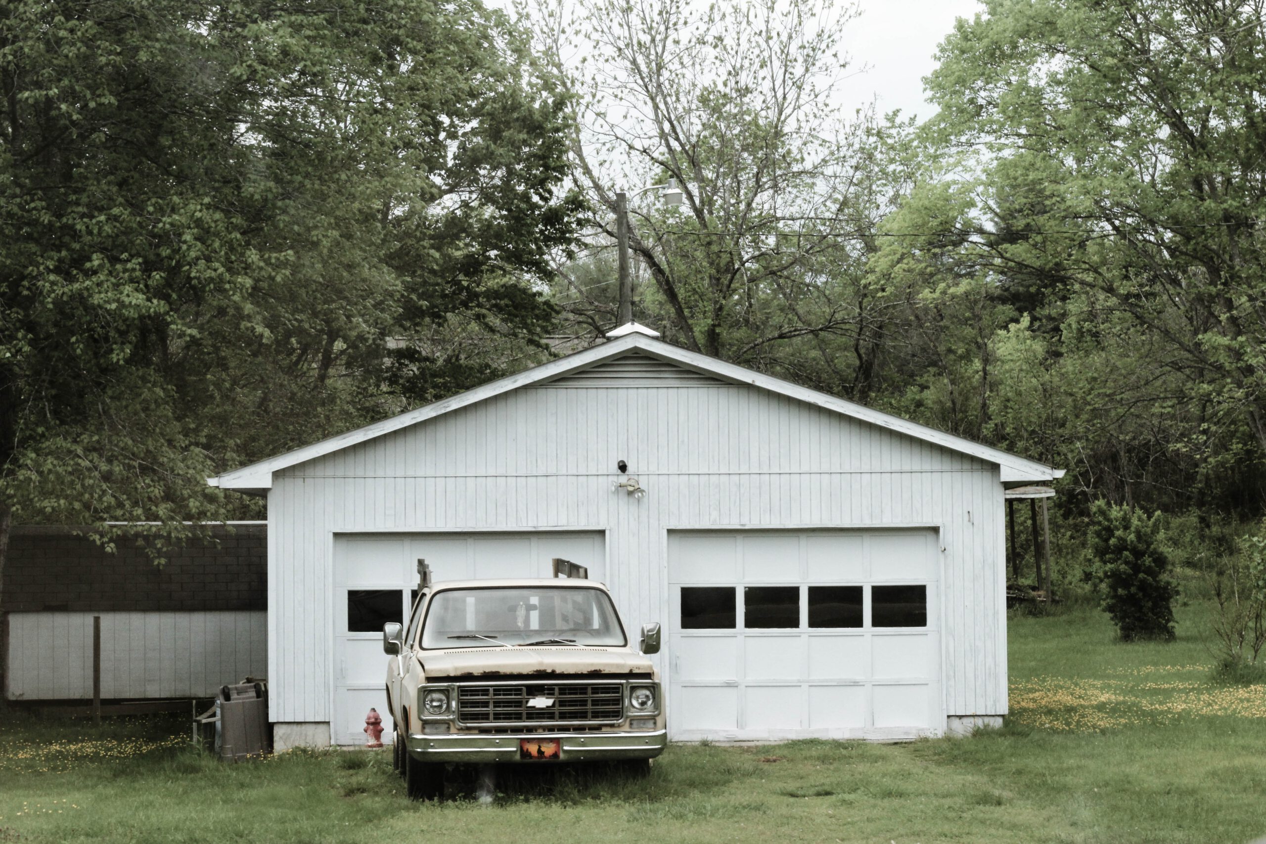 Biały garaż wolnostojący i stary samochód stojący przed nim